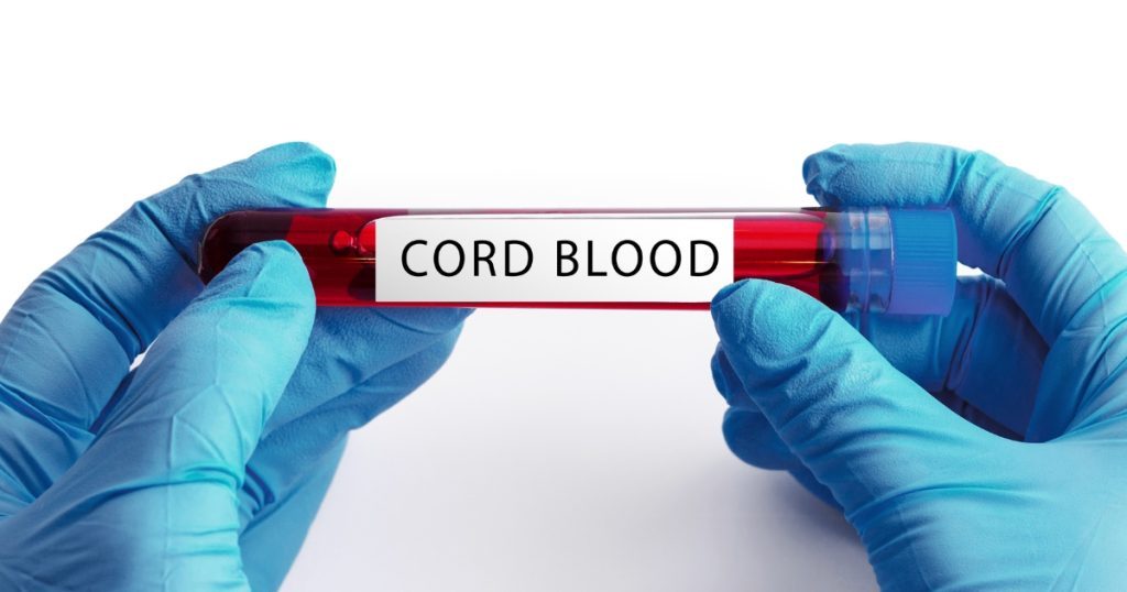Gloved hands holding a sample tube labeled cord blood.