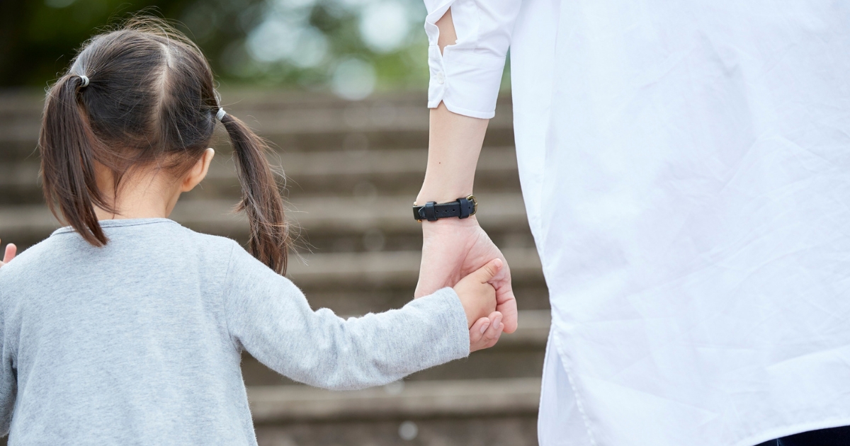 Parent holding a young girl's hand while walking up steps.